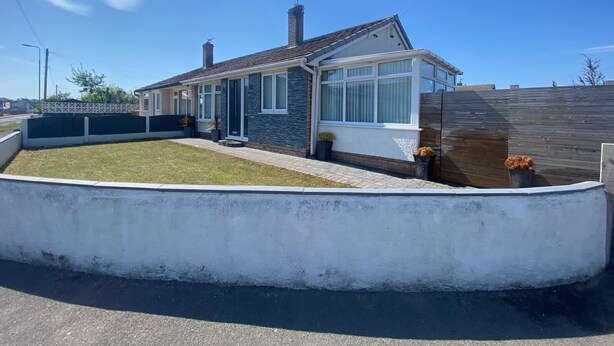 Una casa moderna de dos pisos con fachada de piedra, ventanas grandes y un patio trasero cercado.