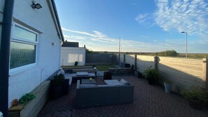 Un patio con mobiliario exterior, vistas al campo y un edificio blanco con una ventana.