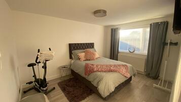 A bedroom with a bed, exercise bike, and a window with curtains.