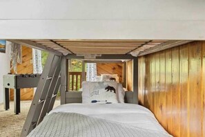 A bedroom with a bunk bed, wooden walls, a ladder, and a window with a view of trees.