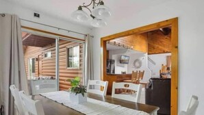 Un comedor con una mesa de madera y sillas blancas, una planta en maceta, y vista a una cocina.