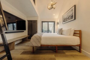 A bedroom with a bed, a bench, a TV, a chandelier, and a window.