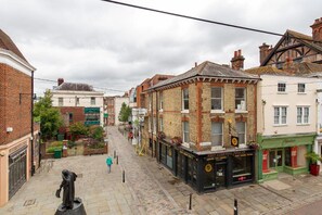 A cobblestone street with historic buildings, a statue, and a closed shop with a 'For Lease' sign.