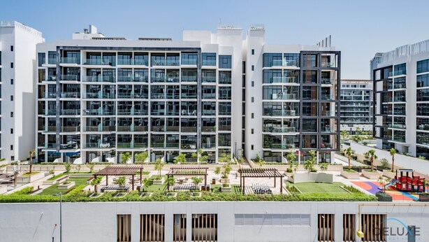 En moderne bygning med flere etager, glasfacade, udendørs siddepladser og en legeplads.