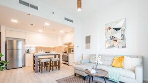 A modern kitchen with white cabinets, a stainless steel refrigerator, and a dining area with stools.