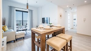 A modern living room with a dining table set for four, a sofa, and a balcony with curtains.