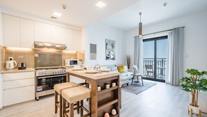 A modern kitchen with a dining area, a large window with curtains, and a balcony.