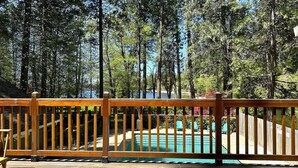 A wooden deck with a pool, surrounded by tall trees.