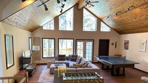 A spacious room with a wooden ceiling, a sofa, a foosball table, and a ping pong table.