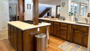 A spacious kitchen with a central island, wooden cabinets, and a stainless steel trash can.