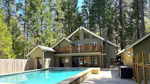 A two-story house with a pool, surrounded by a wooden fence and trees.