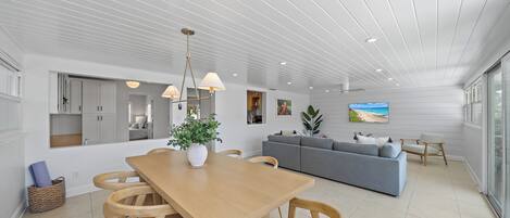 A modern living room with a wooden dining table, grey sofa, and a large window.