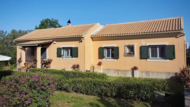A two-story house with a tiled roof, green shutters, and a small porch with potted plants. - Eleni's House by Corfuescapes (Corfu)