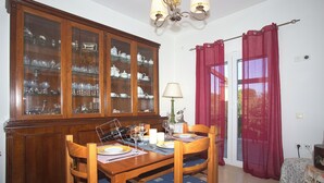 A dining area with a wooden table set for four, a glass cabinet with dishes, and a red curtain. - Eleni's House by Corfuescapes (Corfu)