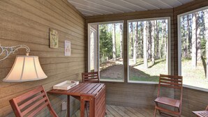 A wooden deck with a table and chairs, a lamp, and a view of a forest through large windows. - Red pine sanctuary with A/C (Mont-Tremblant)