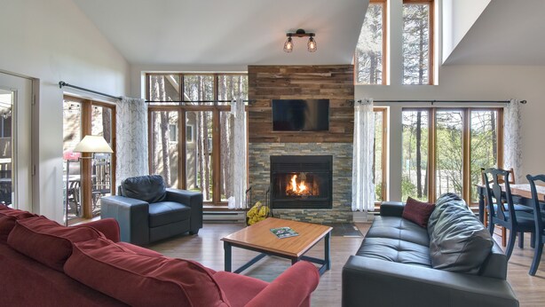 A spacious living room with a fireplace, modern furniture, and large windows offering a view of the outdoors. - Red pine sanctuary with A/C (Mont-Tremblant)