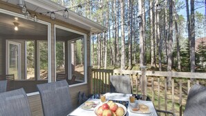 A covered outdoor seating area with a table set for breakfast, surrounded by a wooden deck and tall trees. - Red pine sanctuary with A/C (Mont-Tremblant)