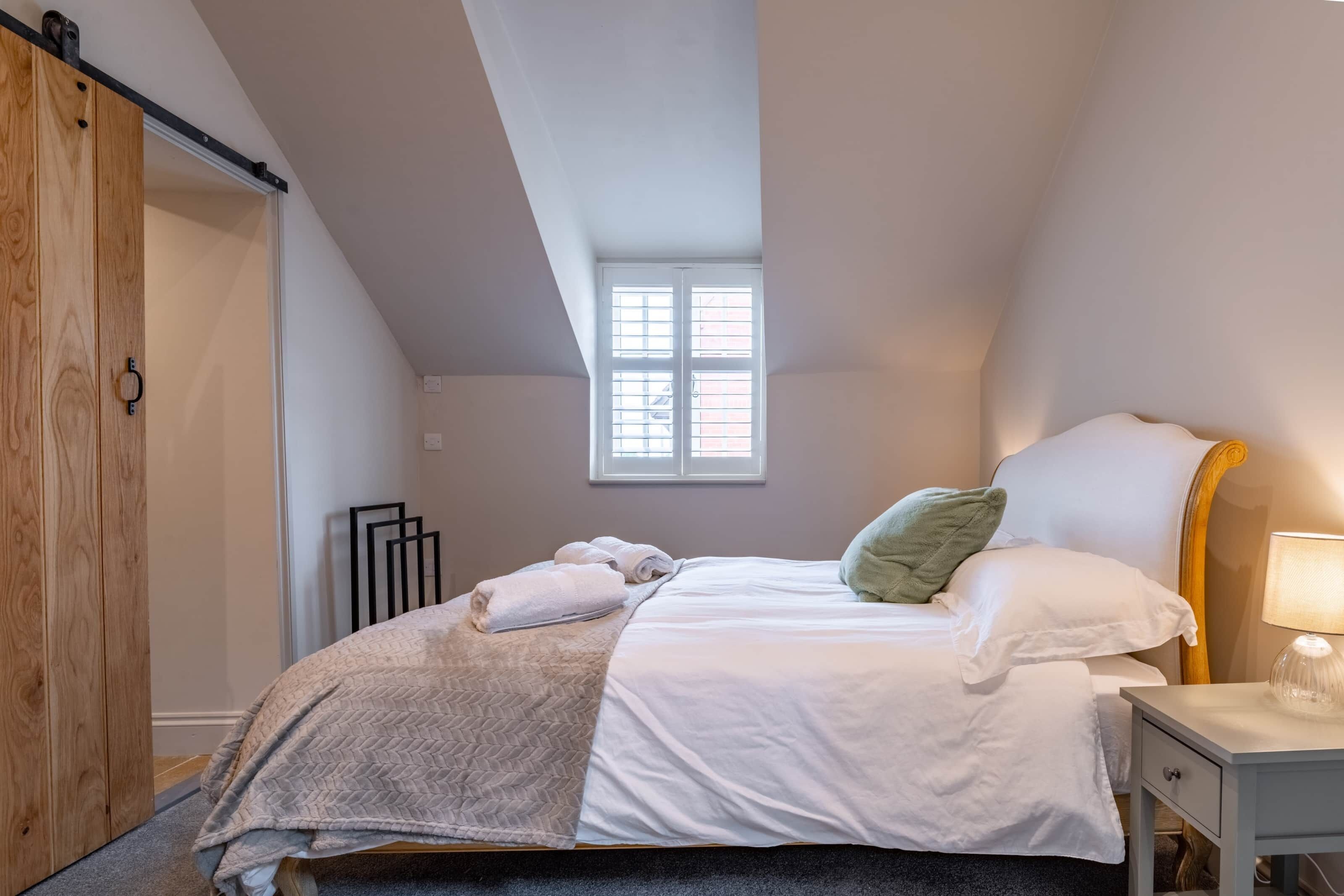 A bedroom with a bed, a nightstand, a window, and a wooden wardrobe.