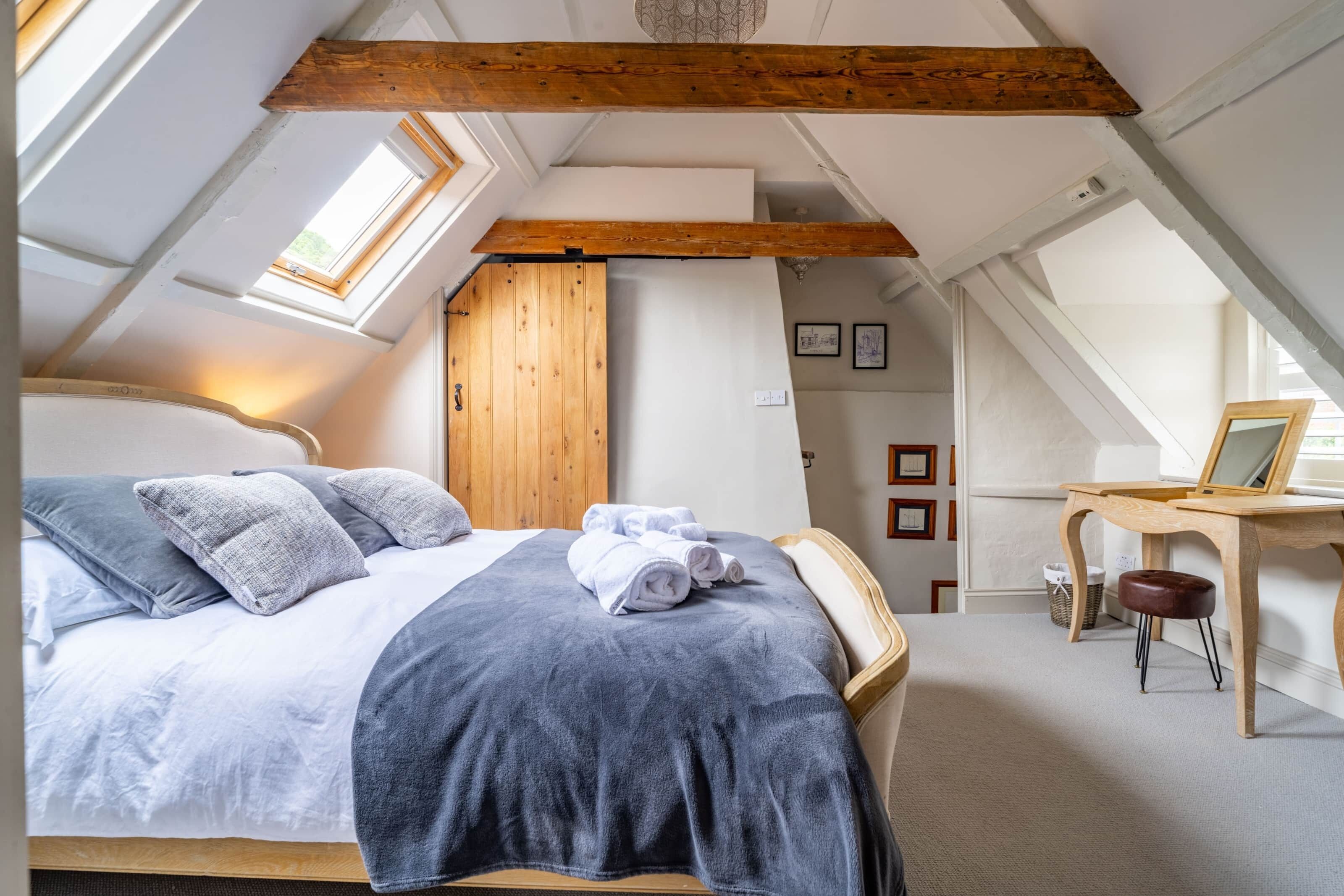 A bedroom with a large bed, wooden beams, a desk, and a chair.