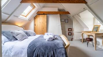 A bedroom with a large bed, wooden beams, a desk, and a chair.
