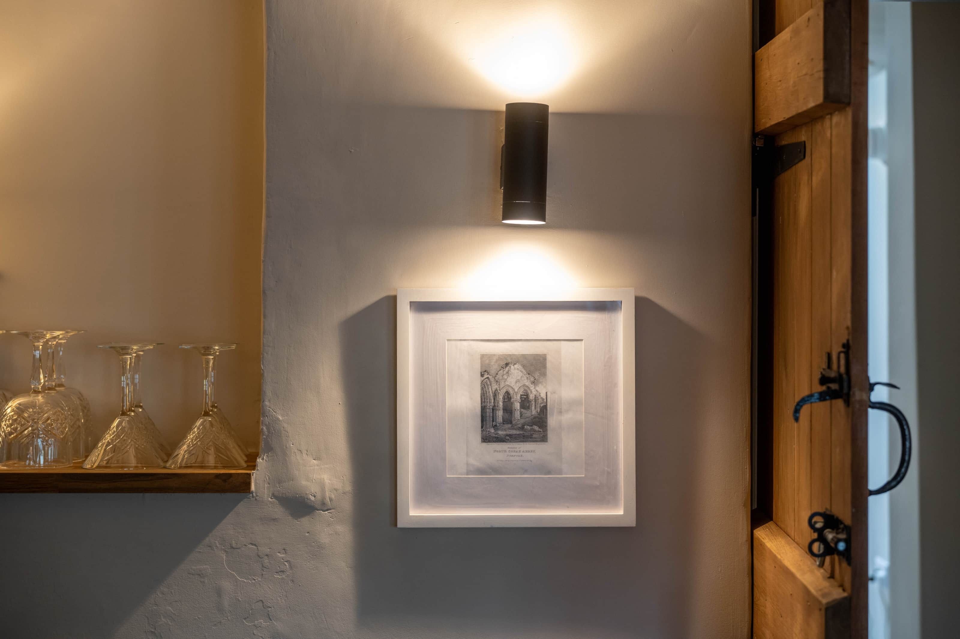 A framed picture on a wall, a shelf with glassware, and a wooden door with a handle.