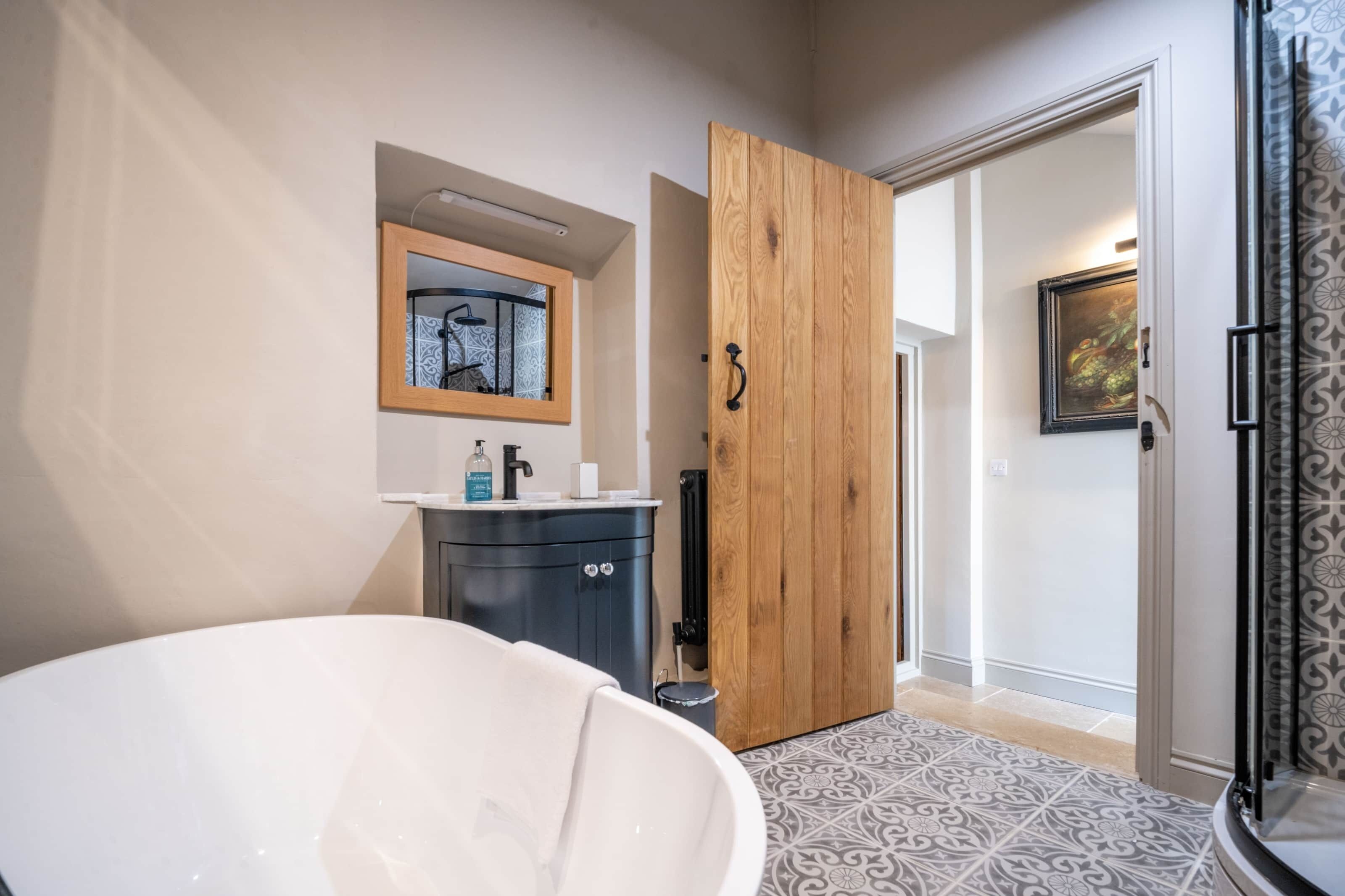 A modern bathroom with a freestanding bathtub, a wooden door, a mirror with a bicycle artwork, and a patterned floor.