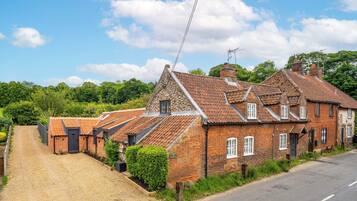 A traditional brick house with a gravel driveway and a road beside it.