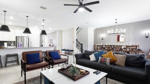Ein modernes Wohnzimmer mit einer Couch, Sesseln, einem Couchtisch und einem Essbereich mit einer Kronleuchter.