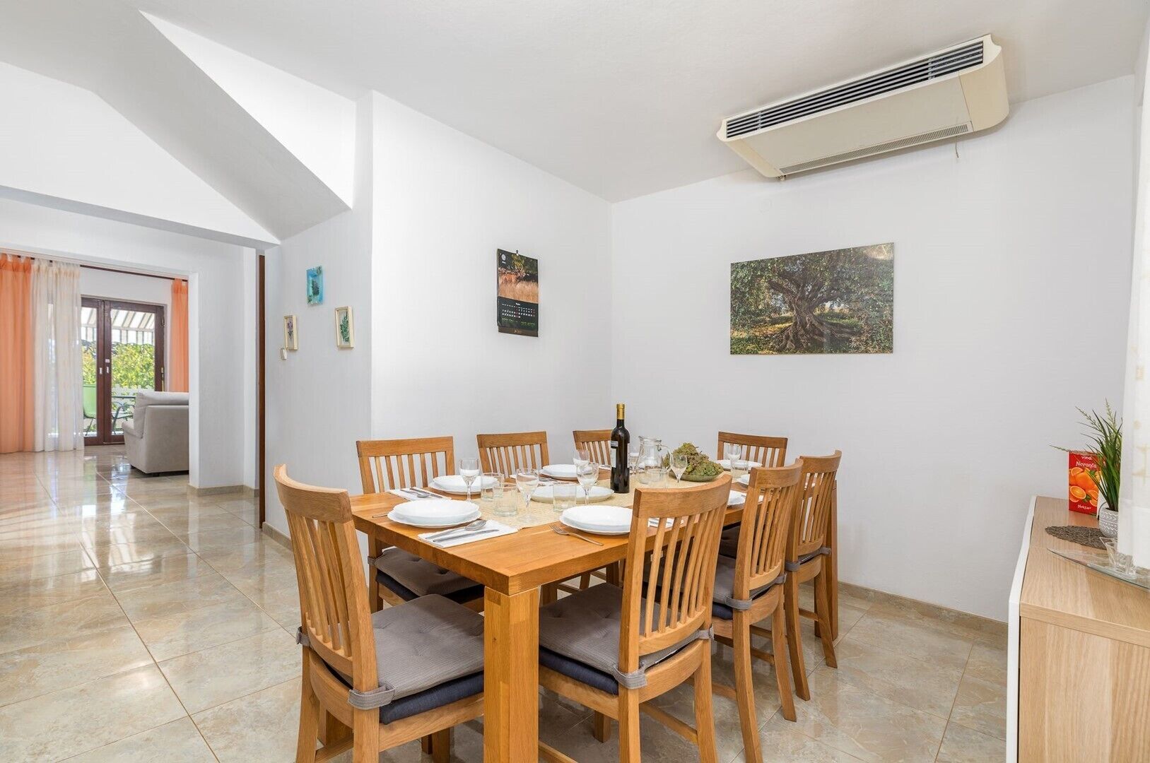 Un coin repas avec une table en bois dressée pour six personnes, entourée de chaises en bois dotées de coussins.