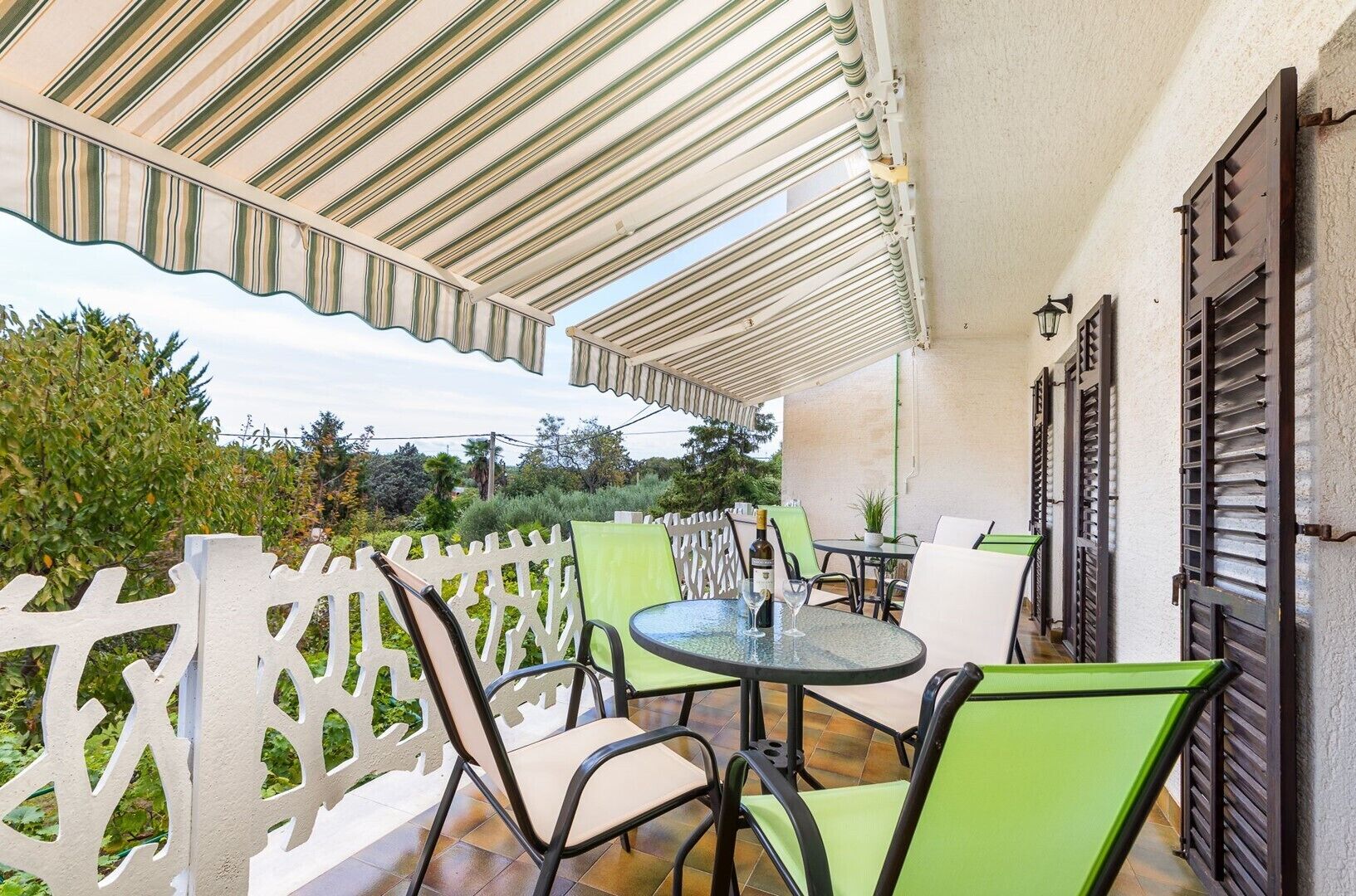 Een terras buiten met een overdekte zithoek, inclusief een tafel en stoelen, en een decoratieve witte hek.