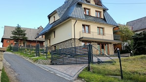 A two-story house with a sloped roof, a stone foundation, and a gated entrance. - Cozy 3-Bedroom Apartment for 5-6 guests with mountain views, with free parking (Zakopane)