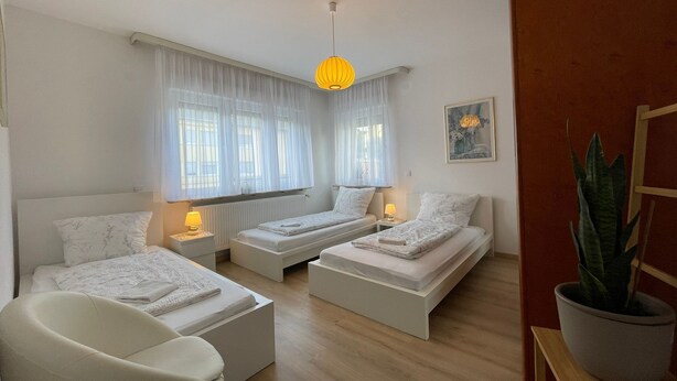 A modern bedroom with two beds, a chair, a potted plant, and a painting on the wall. - 5 Minuten von Koblenz Uni Entfernt Ferienwohnung (Koblenz)