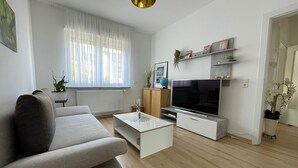 A modern living room with a grey sofa, a coffee table, a TV on a stand, and a window with sheer curtains. - 5 Minuten von Koblenz Uni Entfernt Ferienwohnung (Koblenz)