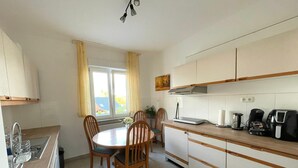 A compact kitchen with a dining table, chairs, a sink, and a window with curtains. - 5 Minuten von Koblenz Uni Entfernt Ferienwohnung (Koblenz)