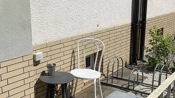 Een buitenruimte met een tafel en stoelen, een klein raam met planten en een metalen hekwerk.