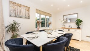Un coin repas avec une table blanche dressée pour six personnes, entourée de chaises à l’assise rembourrée de couleur bleu foncé.