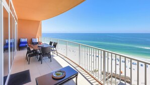Un balcón con mesa y sillas, con vista a una playa de aguas azules cristalinas y arena dorada.