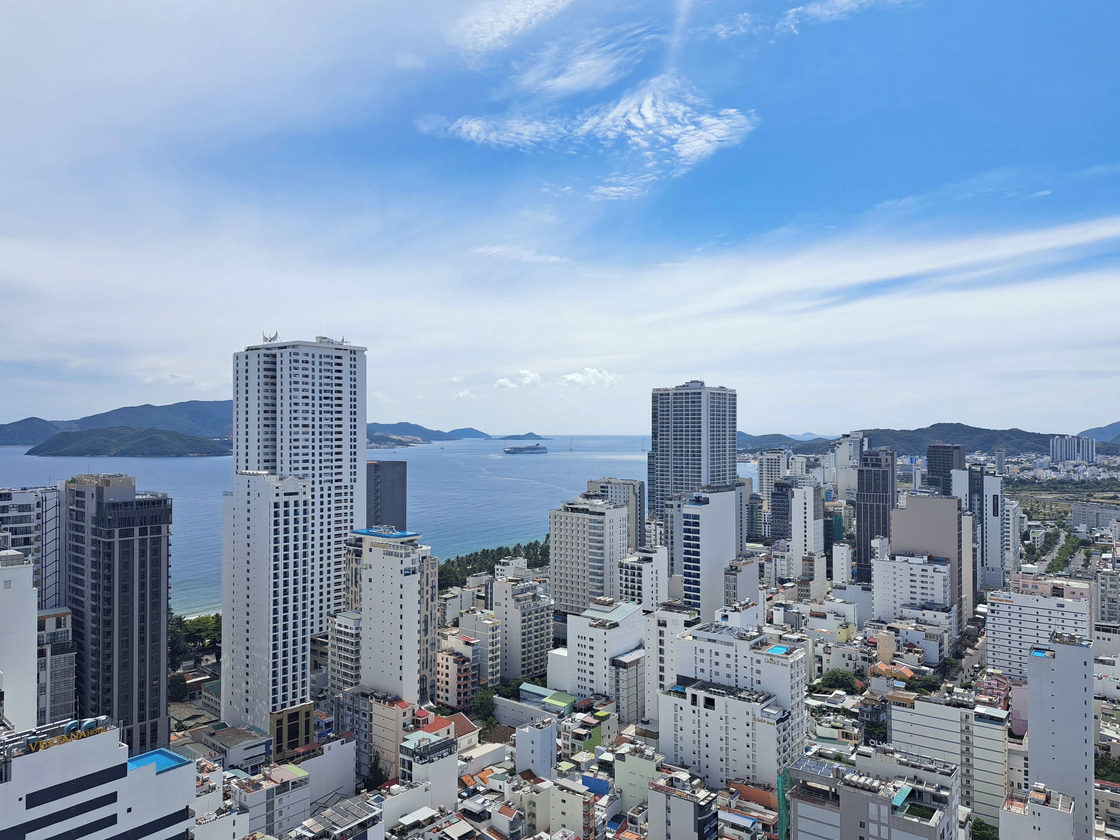 A cityscape with high-rise buildings, a body of water, and distant mountains.