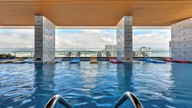 A pool area with clear water, lounge chairs, and a view of the city skyline. - S Lux Apartment Virgo Nha Trang (Nha Trang)