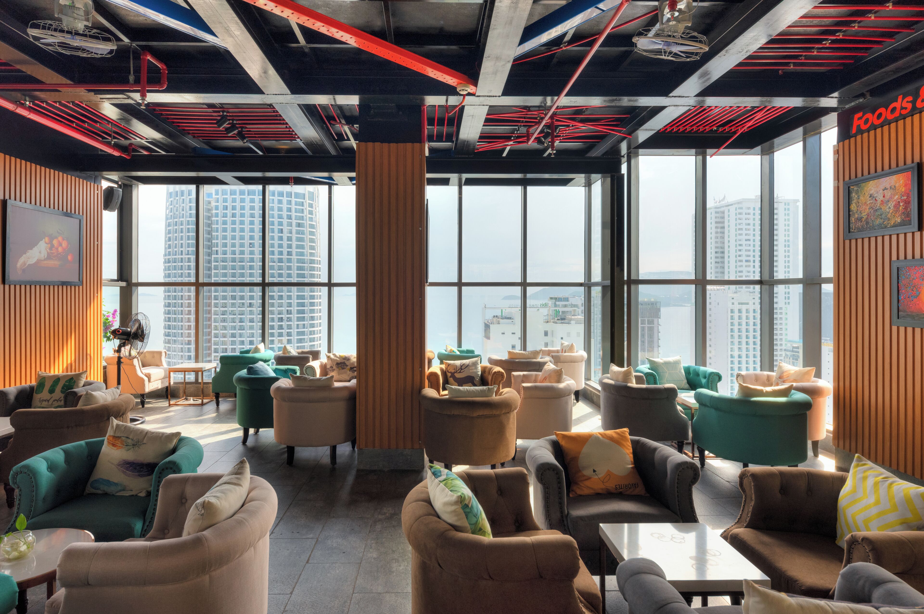A modern lounge with multiple seating areas, large windows offering city views, and exposed industrial ceiling elements.