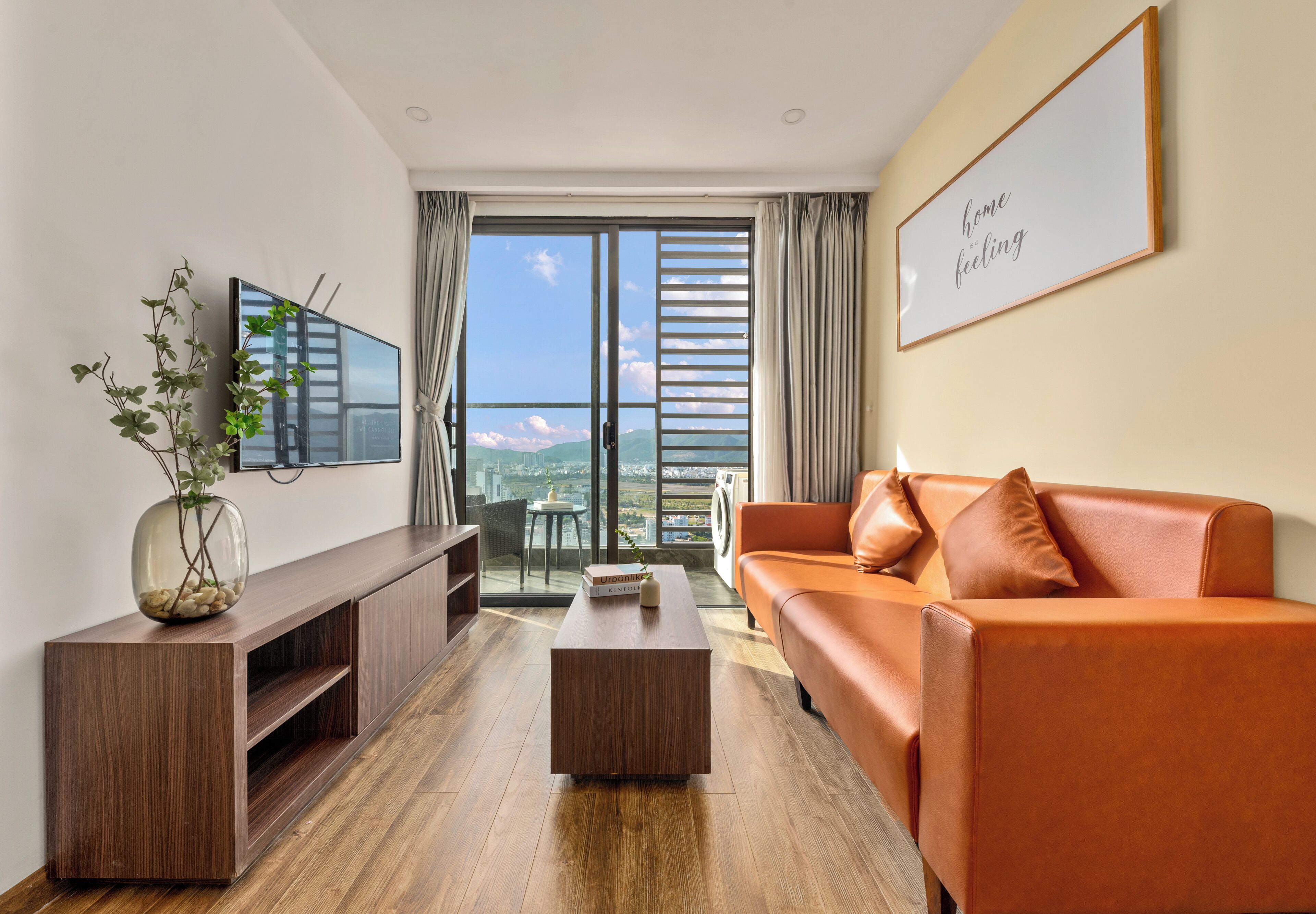A modern living room with a wooden entertainment unit, a leather sofa, and a view of the city through large windows.