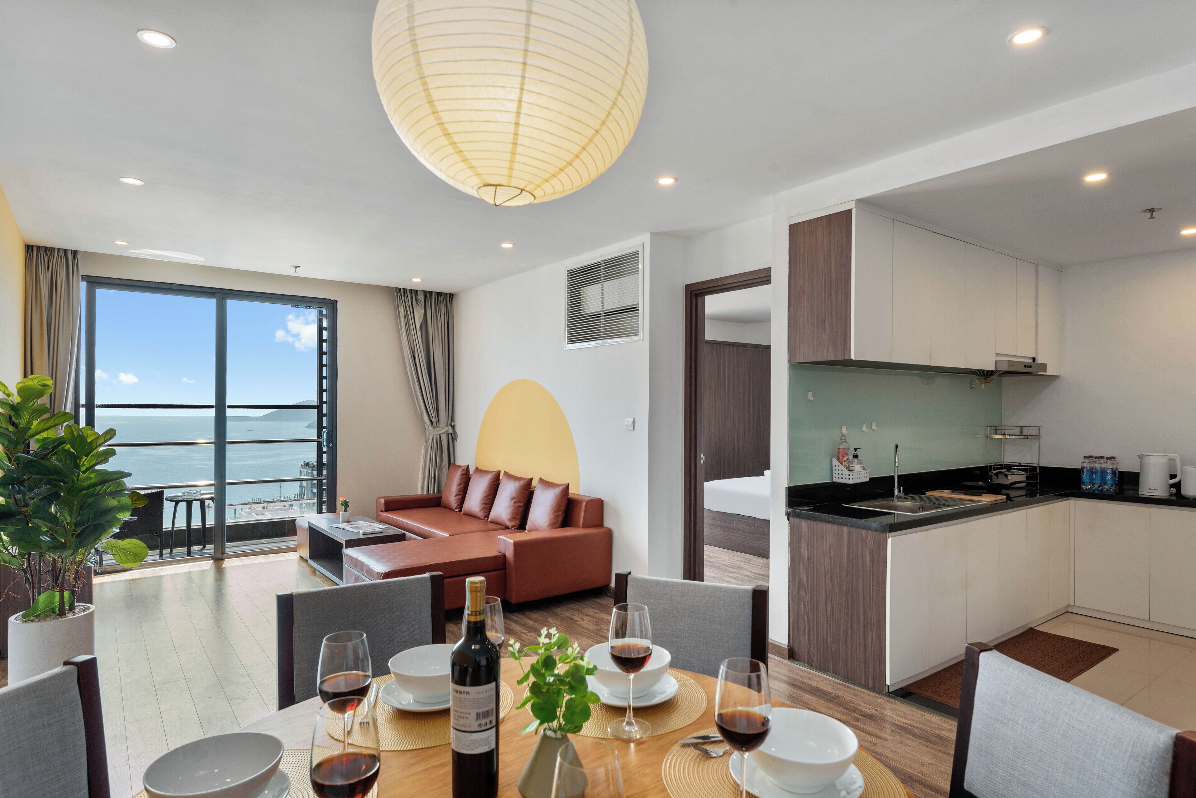 Quarto de hotel moderno com área de refeições, cozinha e sala de estar com vista para o mar.