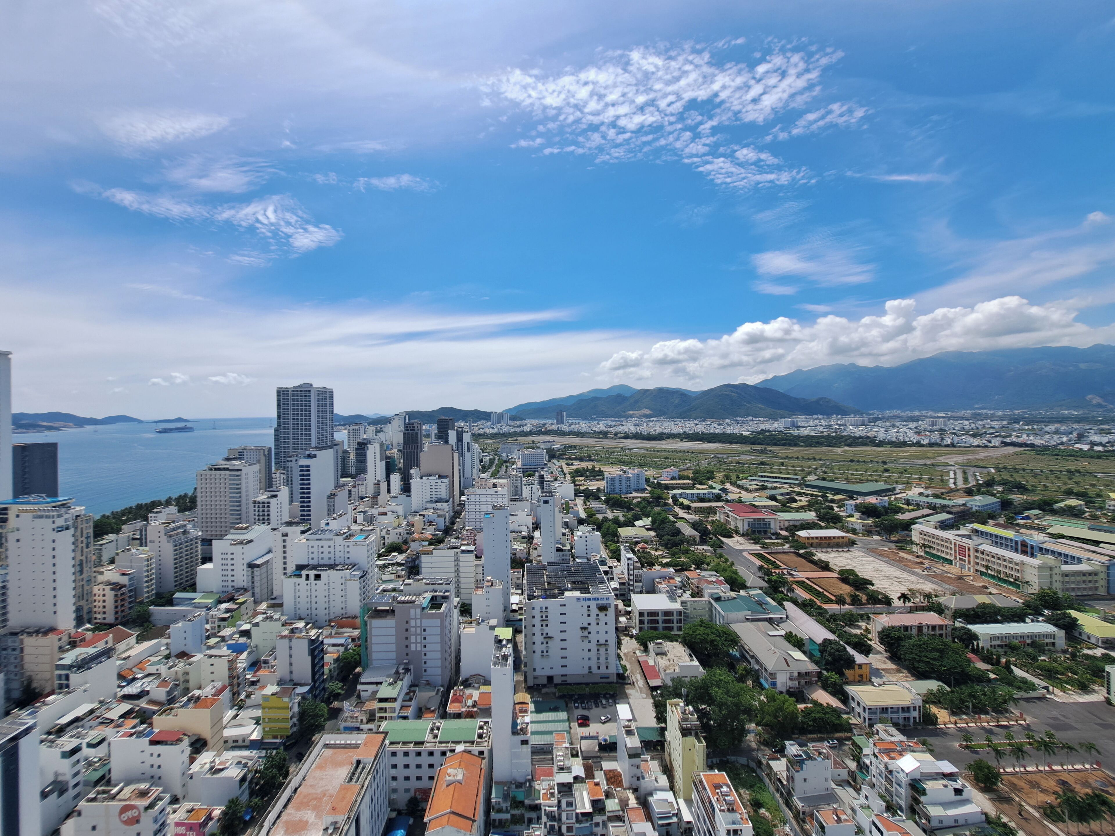 A cityscape with high-rise buildings, a body of water, and mountains in the background.