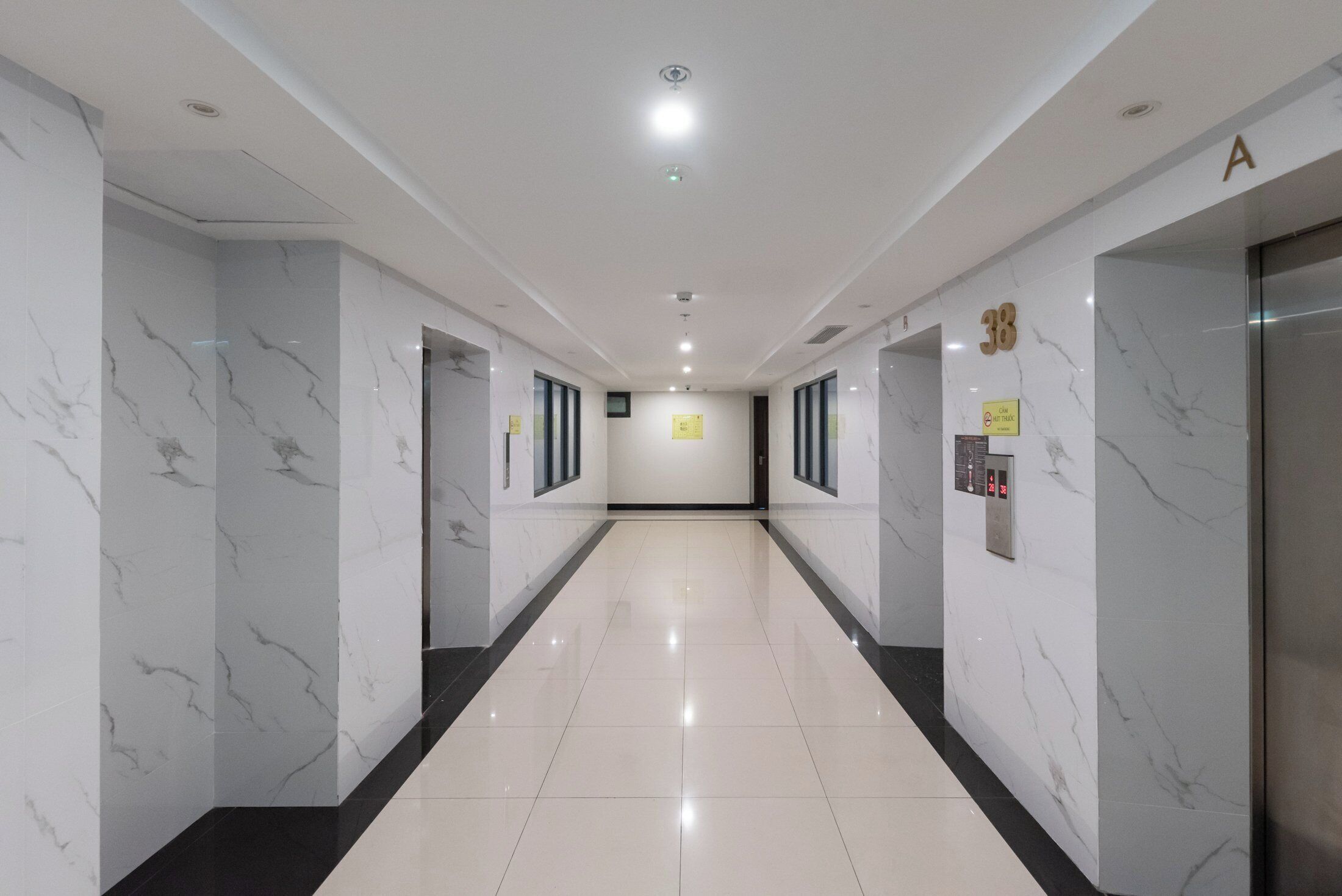 A modern hotel corridor with marble walls, a shiny tiled floor, and an elevator on the right.