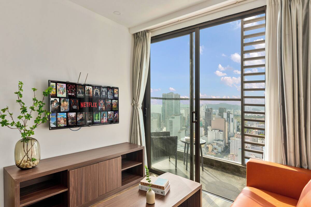 Un salon moderne doté d’une grande fenêtre, d’un écran Netflix fixé au mur, d’une console en bois et offrant une vue sur le paysage urbain.