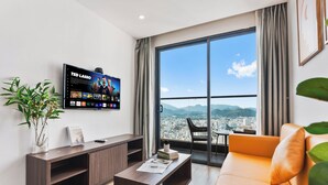 A modern living room with a large TV, a sofa, a coffee table, and a view of a cityscape through a large window. - S Lux Apartment Virgo Nha Trang (Nha Trang)