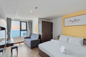 A modern hotel room with a large bed, a desk, a chair, and a view of the ocean. - S Lux Apartment Virgo Nha Trang (Nha Trang)