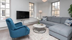 A modern living room with a grey sofa, a blue armchair, a round coffee table, and a flat-screen TV. - Stylish 2-bed apartment in the heart of Bath - Pass the Keys (Bath)