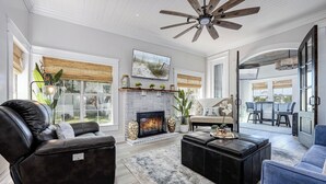 A spacious living room with a fireplace, leather sofa, and a ceiling fan. - Oak & Ocean * Pet Friendly, Boat Launch, Firepit, Hot Tub, Grill (Santa Rosa Beach)
