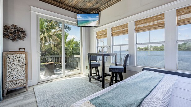 A bedroom with a large bed, a TV on the wall, and a view of the beach. - Oak & Ocean * Pet Friendly, Boat Launch, Firepit, Hot Tub, Grill (Santa Rosa Beach)